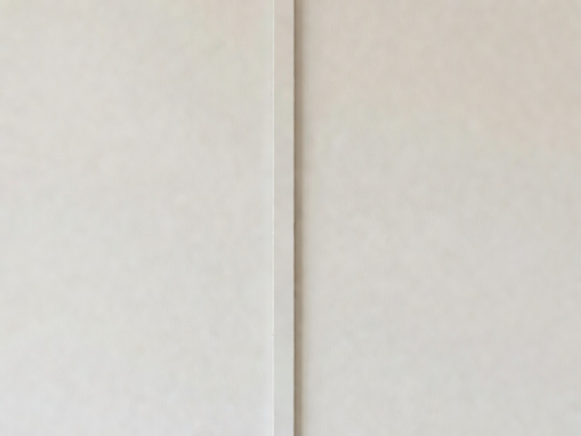 Close-up of a slim painted cable channel running down a plaster wall, almost invisible against the paint